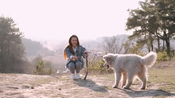 Pretty Girl Is Walking with a Cute Fluffy Dog in the Field