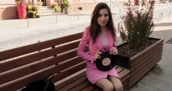 Pretty brunette in pink sitting on a bench with a disk in the city