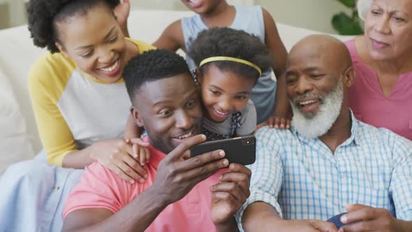 Happy african american family sitting and using smartphone in living room