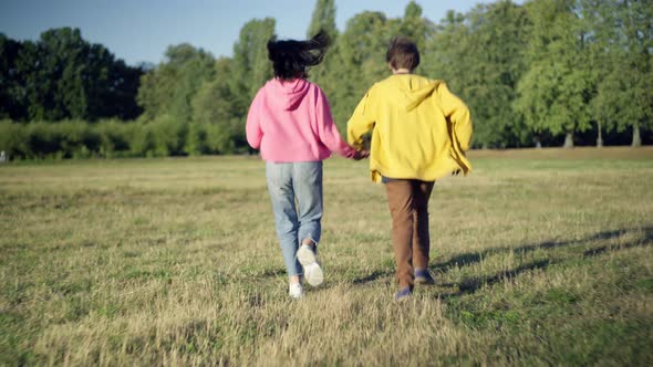 Live Camera Follows Excited Happy Teenage Couple Running on Sunny Summer Lawn Holding Hands