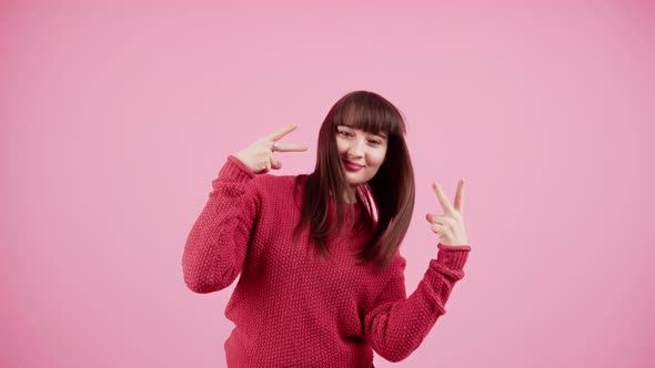 Young Caucasian Woman with Windblown Brown Hair Wearing Red Knitted Sweater While Showing Vsign with