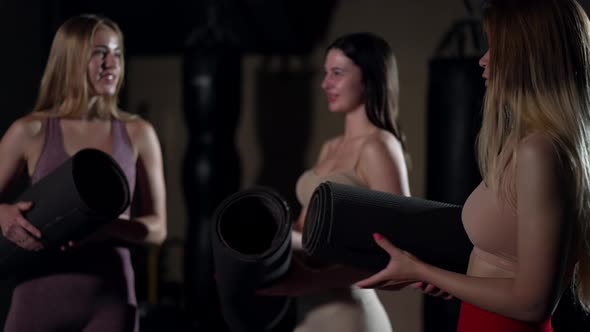 Side View Confident Young Woman Talking with Blurred Friends Standing with Exercise Mat in Gym