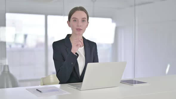 Busy Young Businesswoman Putting Finger on Lips in Office 