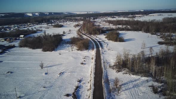 Aerial view of an asphalt road surrounded by snow in the countryside.