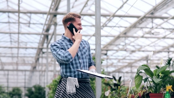 Young Man Talking On The Phone In Greenhouse. alt