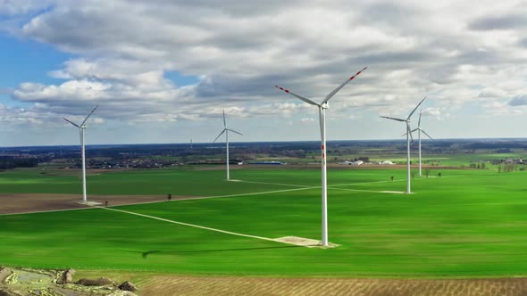 Wind turbines with blue sky and clouds on green field, aerial view