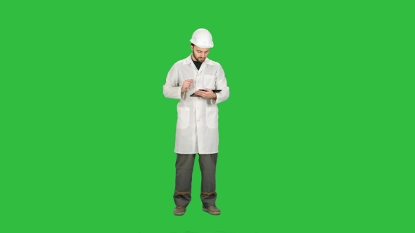 Technician Building Site Using Tablet To Check Progress On a Green Screen, Chroma Key.