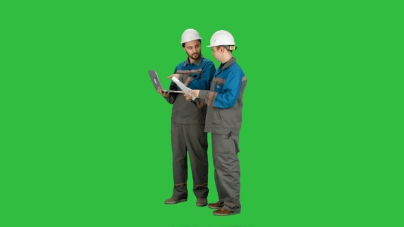 Two Experienced Industrial Technicians Work On Laptop On a Green Screen, Chroma Key.