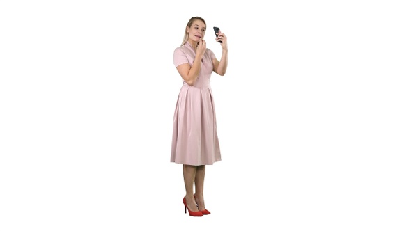 Woman applying lipstick looking at her phone on white background.
