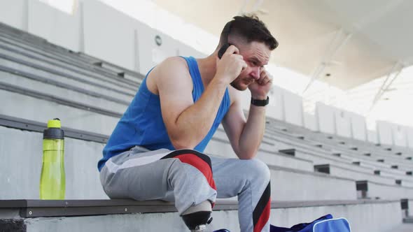 Caucasian disabled male athlete with prosthetic leg sitting, wearing headphones