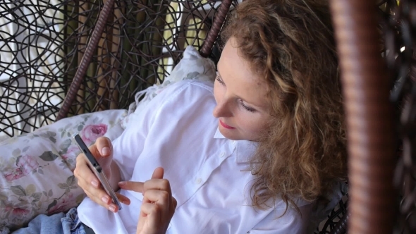 Relaxed Casual Woman Using Mobile Phone And Swinging In Chair