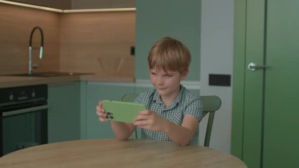 Boy Playing Video Game Using Mobile Phone Sitting at Home