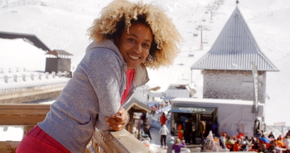 Smiling Woman Leaning On Railing At Ski Resort alt
