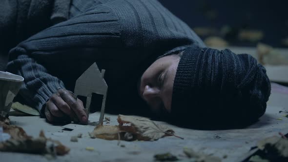 Freezing Refugee Sleeping on Street and Holding Paper House, Missing Home