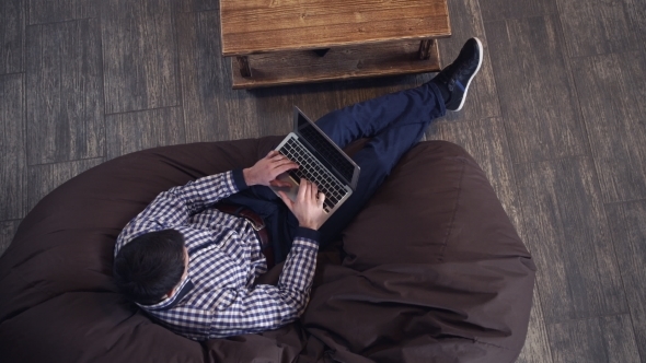 Man Lying In An Armchair, Holding a Laptop And Typing.