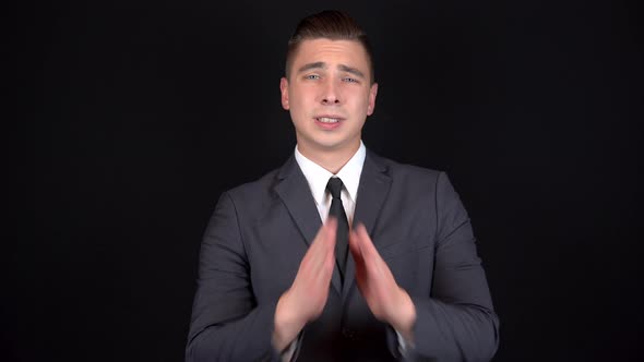 Young Businessman Folded His Hands and Begs. Man in a Black Suit on a Black Background