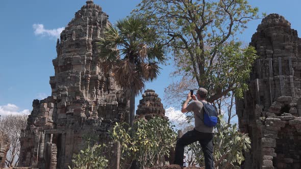 Medium Exterior Shot of a Tourist Photographing an Ancient Temple Structure With Their Phone at Angk