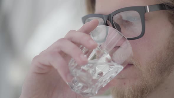 Close Up Portrait of Blond Bearded Thoughtful Man in Glasses Drinking Water From the Glass Close Up