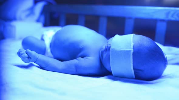 Newborn Having a Treatment for Jaundice Under Ultraviolet Lamp in Home Bed