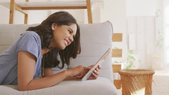 Beautiful woman using digital tablet while laying on the couch