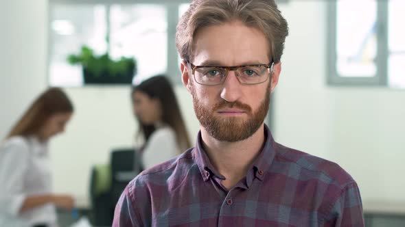 Portrait of a Bearded Guy in Glasses and in a Casual Plaid Shirt Standing in the Office Center in