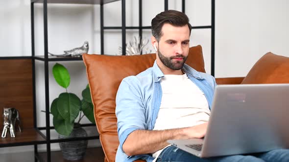A Focused Man Wearing Casual Shirt Using a Laptop Sitting at Home