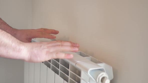 Man Warms His Hands From a Heating Radiator