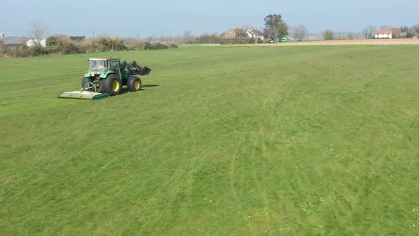 Tractor rear follow level with drone. Hedgerow and fields in view houses in distance HD60