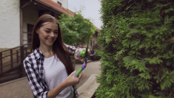 Smiling Lady Cutting Overgrown Branches on Decorative Thuja