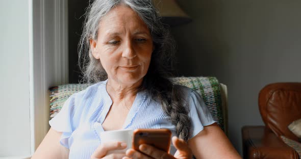 Senior woman having coffee while using mobile phone 4k