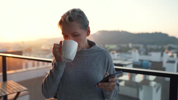 Woman Starts Her Day with a Cup of Tea or Coffee and Checking Emails in Her Smartphone on the