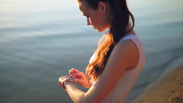 Woman Touching Smartwatch on Beach During Sunset
