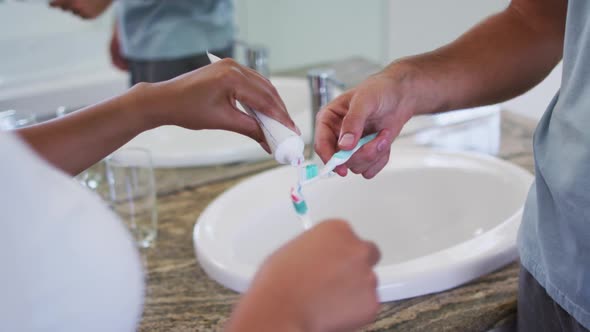 Mid section of mixed race couple putting toothpaste on the brush at bathroom