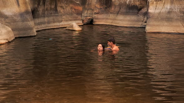 Guy Carries in Arms Girl Helping Swim in Lake Created by Stream