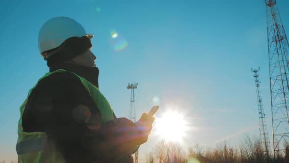 Mature Engineer Working on Smartphone with Satellite Dish Telecom Network on Telecommunication Tower