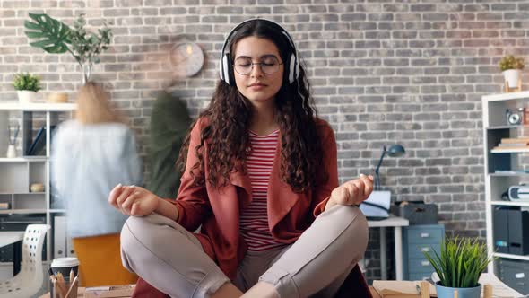 Zoom Out of Lady Listening To Music Relaxing in Office on Table in Lotus Pose