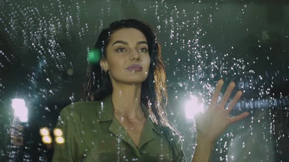 Beautiful Woman Touches the Glass Door with Rain Drops and Smiling