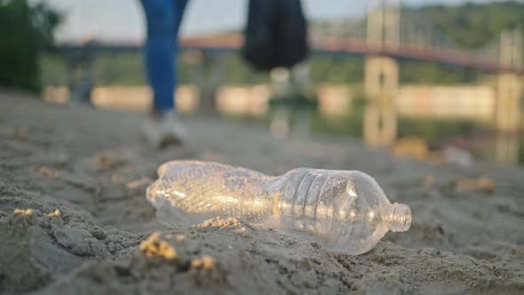 Volunteer Walks on Sand Beach Gathering Bottle in Trash Bag