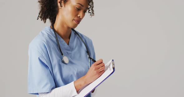 Video of biracial female doctor writing on clipboard on blue background