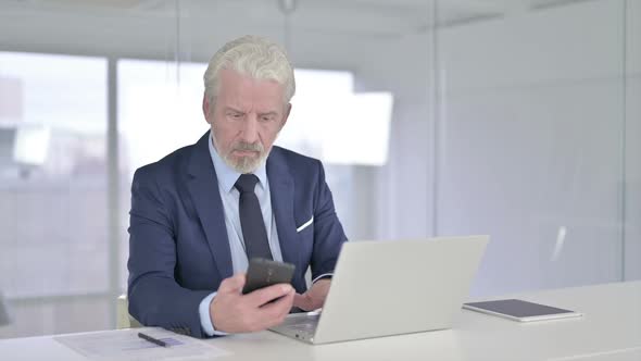 Serious Old Businessman Using Smartphone in Office