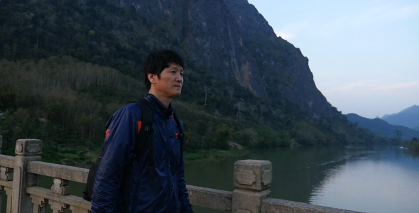 Asian Man Walking on Bridge Passing River