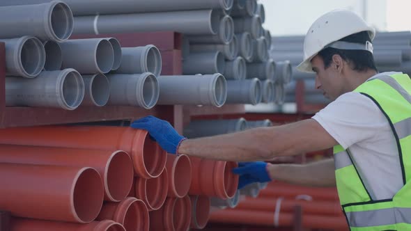 Side View of Concentrated Professional Middle Eastern Man Inspecting Plastic Pipes at Huge Storage