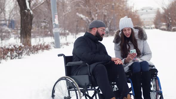 Married couple with disabilities are sitting in wheelchairs, at park winter