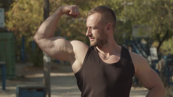 Confident Muscular Man Kissing His Biceps Outdoors