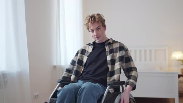 A Young Disabled Man is Riding in His Wheelchair Around the Room and Looking to the Camera