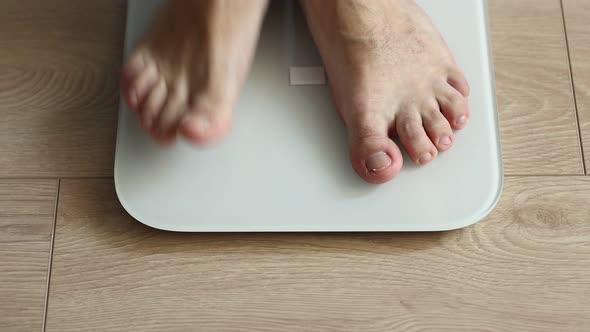 Man weighing himself - male bare feet stepping on white digital floor scales at home: close up view.