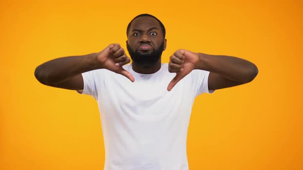 Confident African American Man Giving Harsh Thumbs Down on Yellow Background