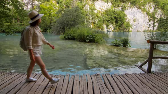 Attractive tourist in a hat walking along a wooden path along the lake. Plitvice Lakes