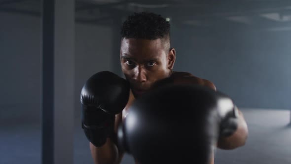 African american man wearing boxing gloves training throwing punches in empty room