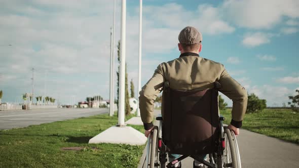 Male Wheelchair User Is Moving Alone on Street Rotating Wheels Back View
